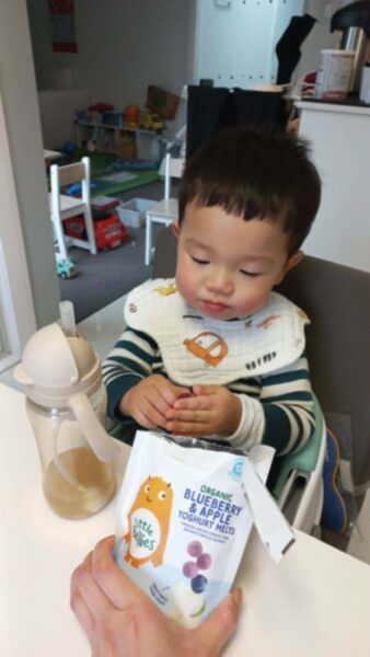 Young toddler sitting in a high chair eating the Little Bellies snacks.