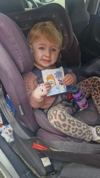 Young child sitting in their booster seat, smiling at the camera whilst holding their Little Bellies bag. 