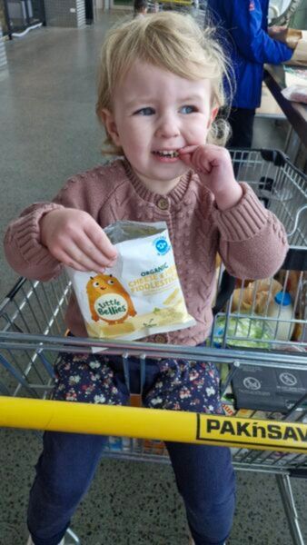 A young child sits in a supermarket trolley eating their Little Bellies snacks. 
