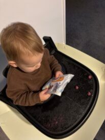 Baby sitting in a high chair looking at a packet of Little Bellies snacks. 