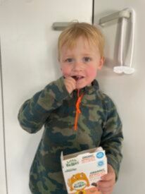 A young child smiles at the camera holding their box of Little Bellies snacks.
