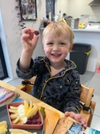 Toddler smiles at the camera whilst holding up their Little Bellies snack ball. 