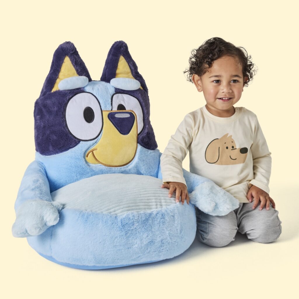 Young child sitting next to a plush chair thats shaped like Bluey.
