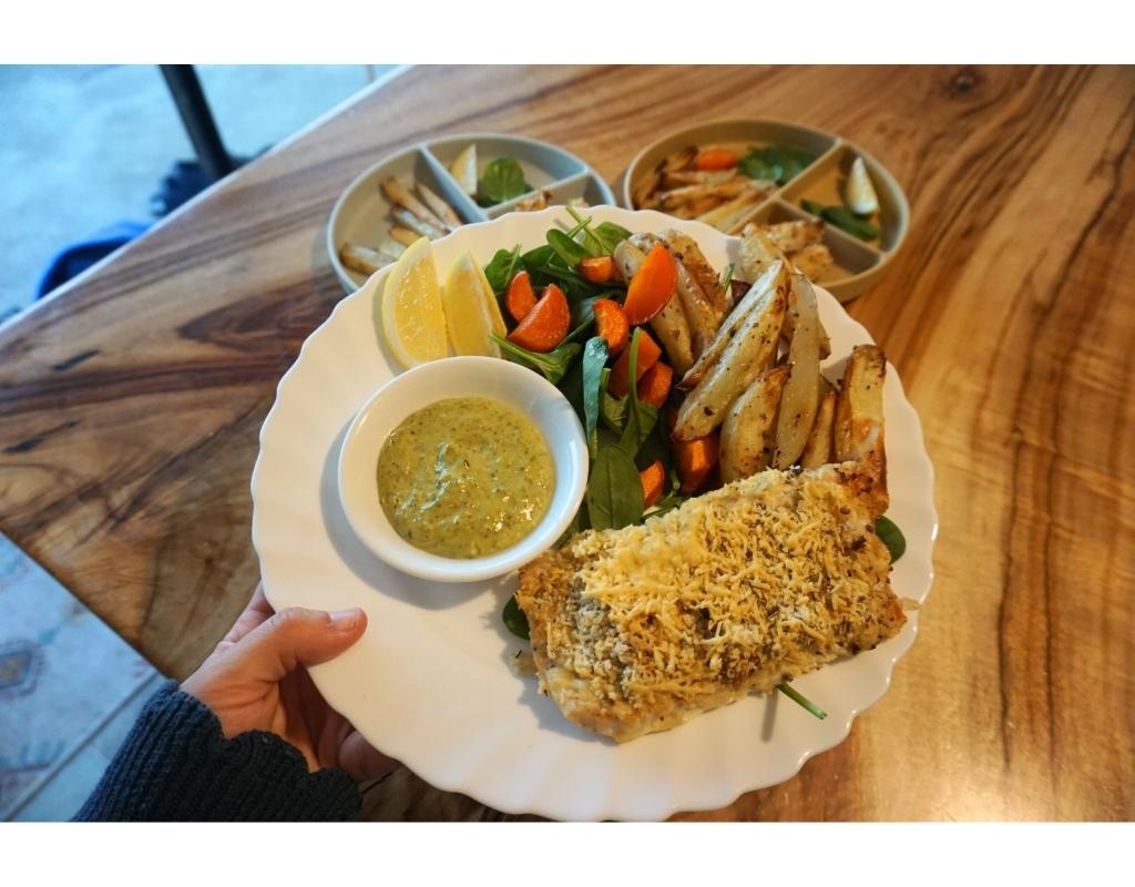 A plate of fish and chips with a salad and dressing.