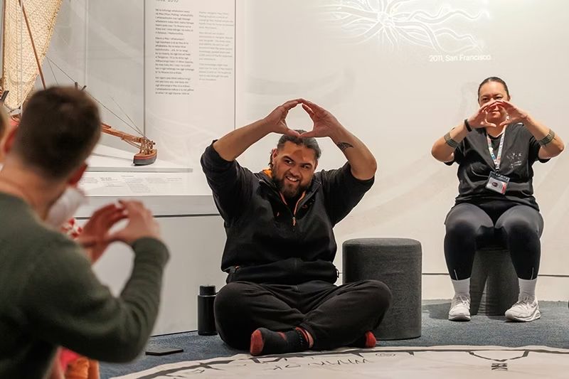 A group sit together practising some New Zealand sign language. 