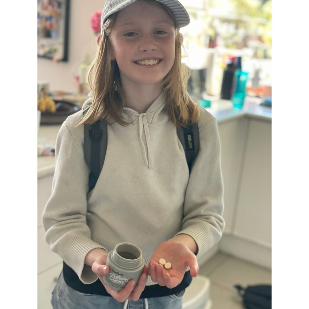 Child smiles at the camera holding the good mood chews tub.
