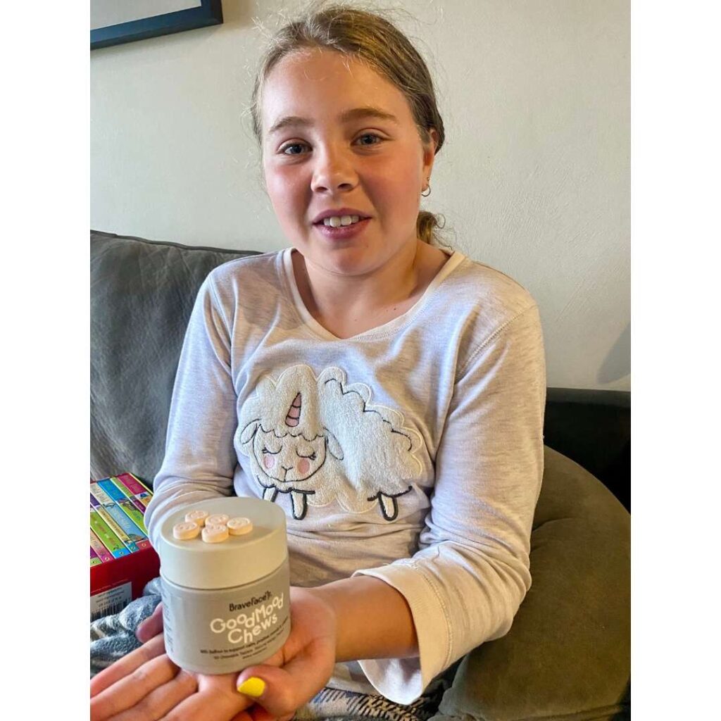 Child smiles at the camera holding the good mood chews tub.