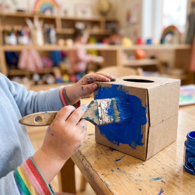 Child painting a tissue box blue.