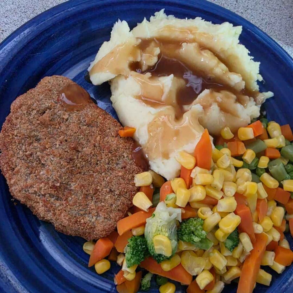 Plate of crumbed schnitzel, mashed potato, and mixed veg. 