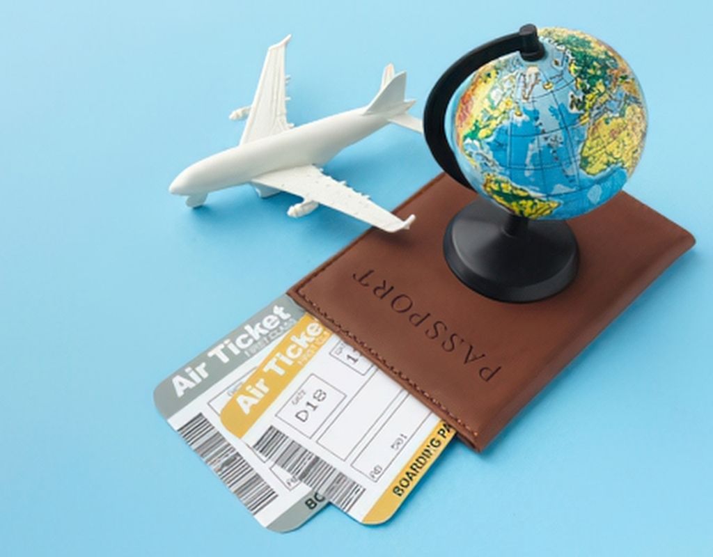 A passport with two tickets sitting next to a toy plane and globe.