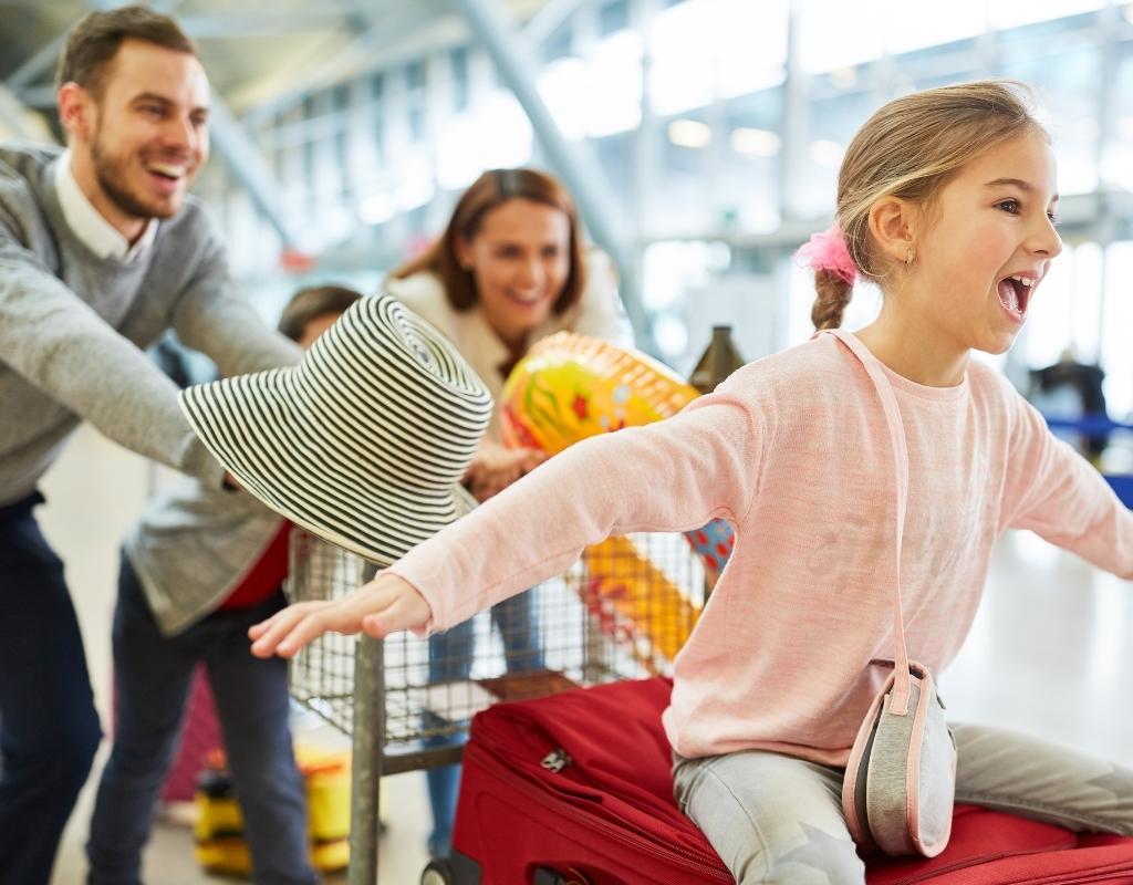 Parents and young child smile as they wheel their luggage through the airport.