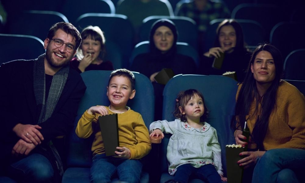 Two parents and their young children sit in the cinema watching a movie. 