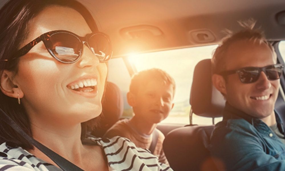Man, woman, and young child sit together smiling in the car. 
