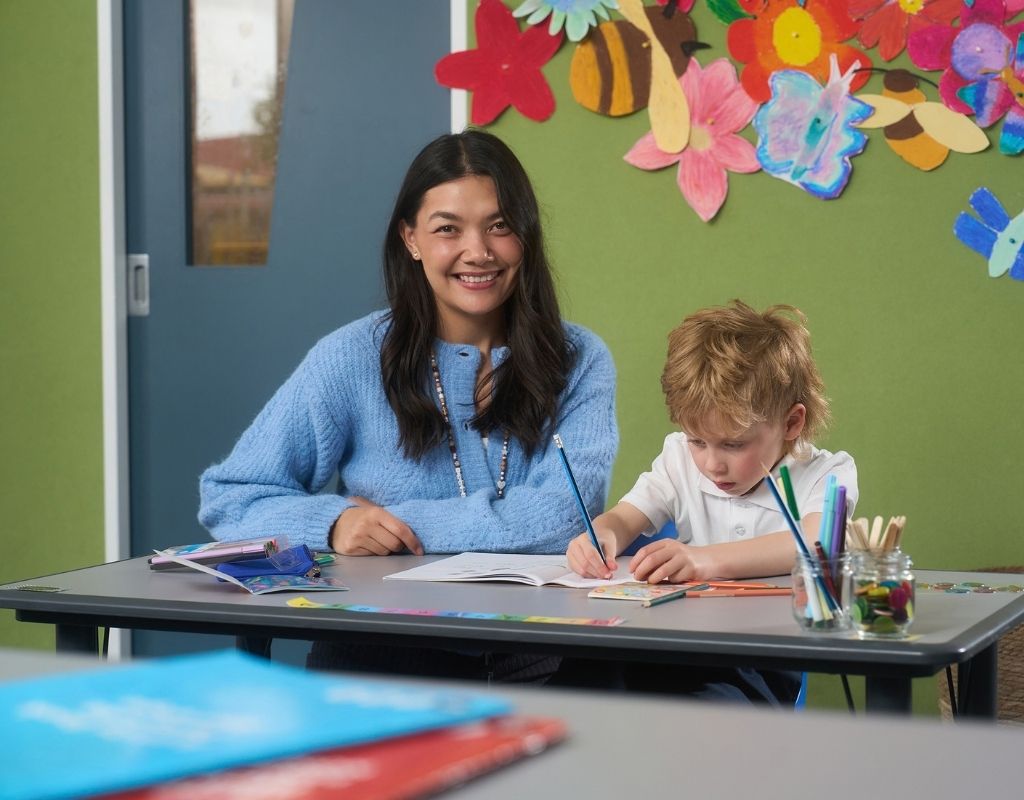 Teacher and student sit together at a desk in the classroom.